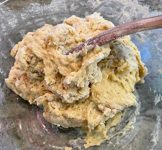 Wooden spoon handle protrudes from rough mass of beige dough.