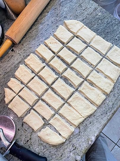 Light colored dough, thin and cut into 32 rectangles, on counter with rolling pin and pizza whieel cutter.
