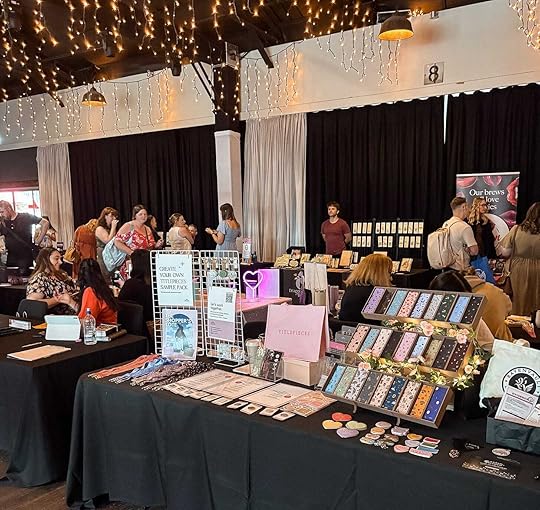 An array of vendors on tables with black table cloths. They are showing their book related wears.