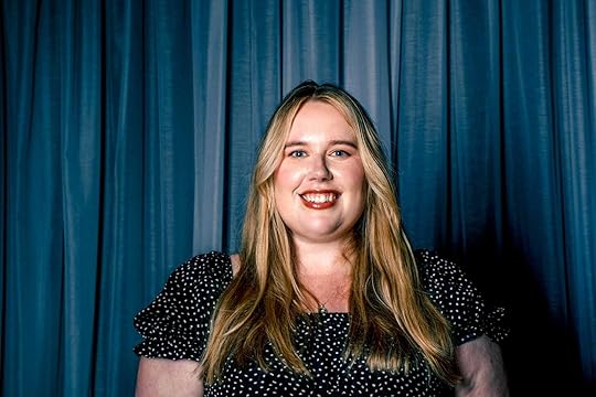 Headshot of MG Hunt. She faces the camera with a blue curtain background behind.