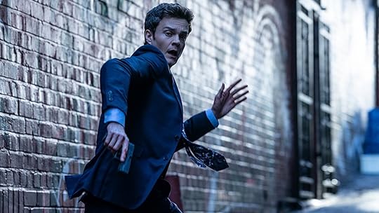 Jack Quaid wearing a suit and running with a gun in Novocaine
