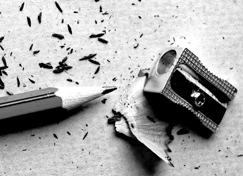 black and white photo of a pencil and sharpener, with pencil shavings. 