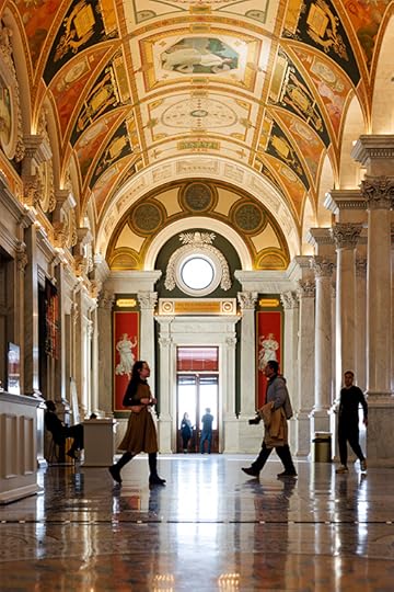 A long view down an ornate, arched hallway in the Library, with a few patrons wlking past.