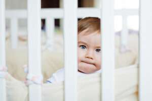 A baby boy's face seen through the slats of his crib, giving an effect of prison bars. | Maria Butrova | Dreamstime.com