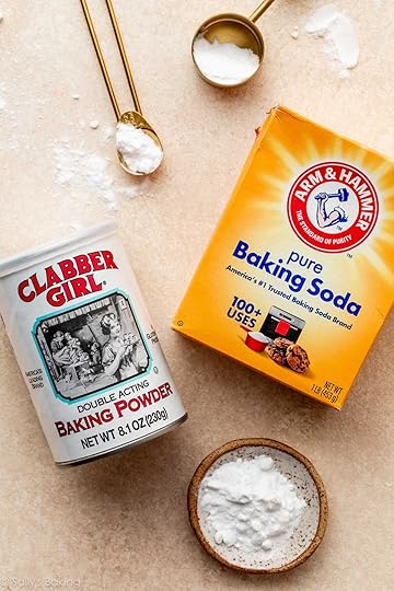 box of baking soda and container of baking powder on peach surface.
