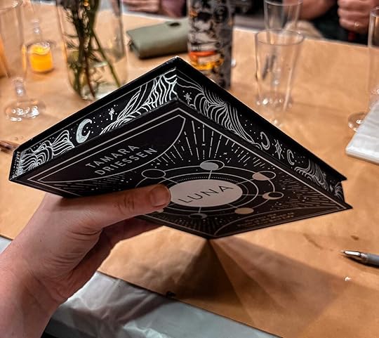 Black and silver book with edges of the pages painted with silver gel pen. MG Hunt is holding the book.