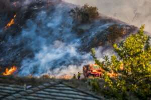 Firefighters stand near a bulldozer as fire burns on a hillside. | Erin Donalson | Dreamstime.com