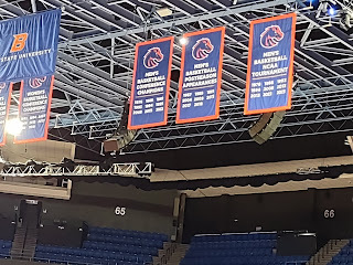 Image of banners hanging from the rafters of an arena. Banners have a Bronco head logo and are blue with white letters, indicating years of championships and tournament appearances.