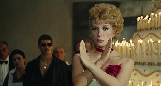 An obvious gay guy and a beautiful showgirl-style blonde stand before a gigantic cake in Fellini's