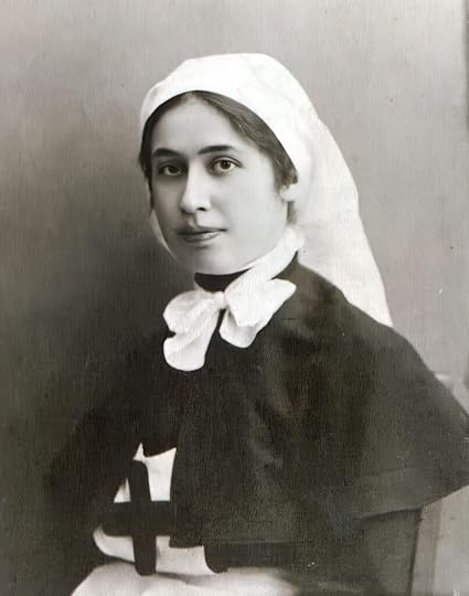Young woman in uniform of a nurse during World War One. She wears a little cape and her head is covered with a white scarf.