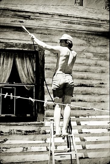 Man painting an old house. He is standing on a ladder wearing cut off jeans and no shirt.