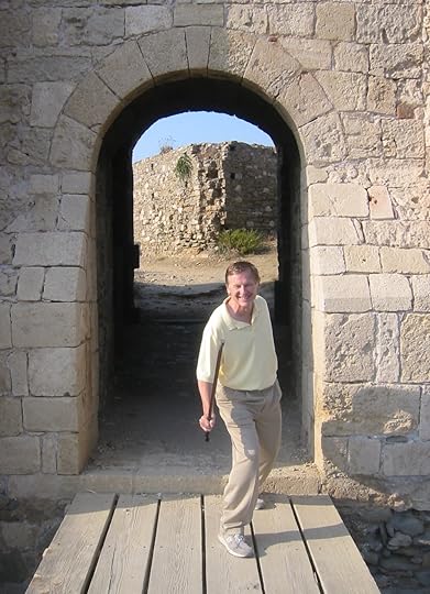 Man posing with fake sword on wooden bridge near arch in old stone wall at Methoni, Greece.