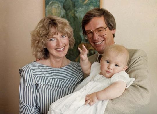 Happy young husband and wife with cute baby in christening gown.