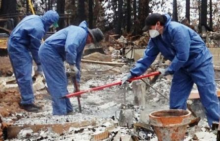3 people in tyvek suits clearing ash after a fire