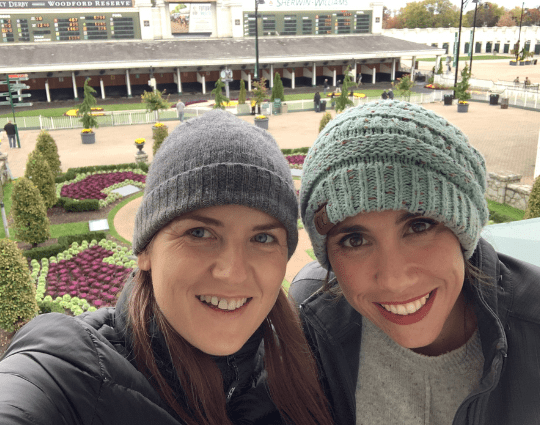 Two women smile for a photo with the Churchill Downs paddock area in the background