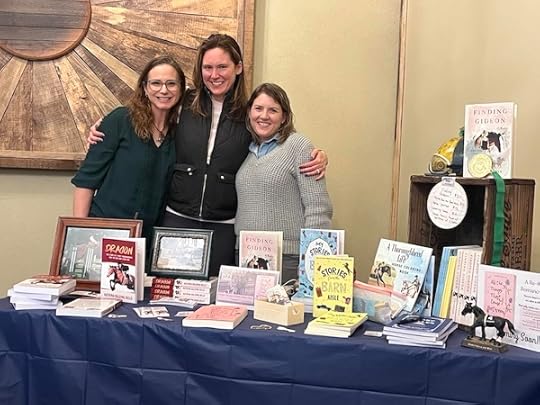 authors Sarah Hickner and Katrina Bills pose with friend Amanda behind a table of books at an expo event