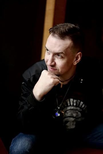 white author in a black t-shirt and jacket, chin on his hand, looking sideways.
