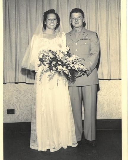 Black-and-white wedding photo of a smiling bride and groom. The bride, in a lace gown, holds a large bouquet. The groom is in a military uniform adorned with decorations. They stand in front of a curtain backdrop, with the groom's hand gently resting on the bride's back.