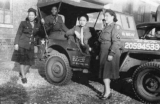 A historical black-and-white photograph showing four women in military uniforms standing and sitting around a World War II-era military jeep. Two women are standing on the right side of the jeep, wearing skirts and military jackets adorned with patches and insignias. One woman is leaning against the front of the vehicle on the left side, while another is seated inside the jeep holding onto its frame. The jeep features a star emblem on the front and military identification numbers on the side.