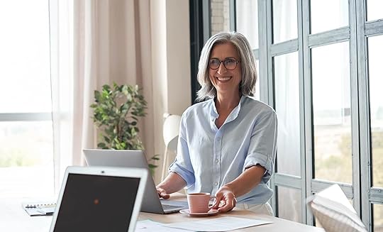 Image of a happy mature woman standing next to a desk working on a laptop. Don't face your treatment-resistant depression alone. With the help of an adult IOP in Houston, TX you can find support to move forward. 