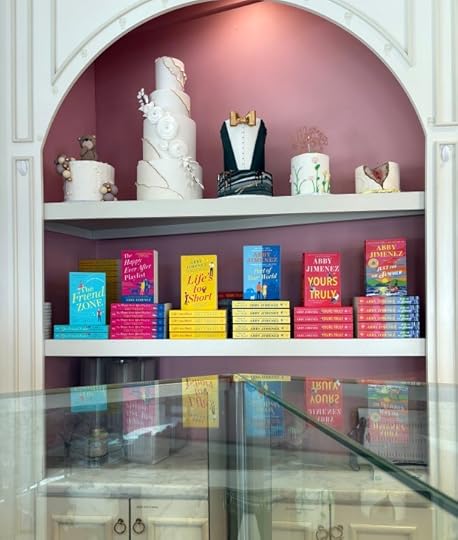 cakes and stacked books in a cupboard, reflected in a glass counter