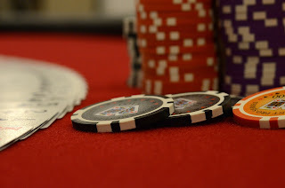 Image of three poker chips (two black, one yellow) spread near fanned out cards, face up. In the background, stacks of poker chips.