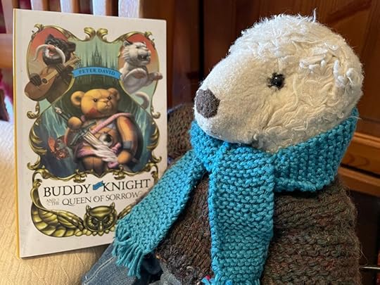 A handsome white teddy bear wearing jeans, a brown knitted jumper and a blue knitted scarf, poses with his copy of Buddy the Knight.