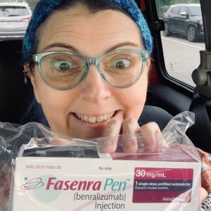 Me grinning like an idiot in my car holding up the box with my Fasenra injector in it when I arrived at my doctor appointment.