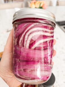 Marie holding up a jar of pickled onions made from her Quick Pickled Red Onion Recipe