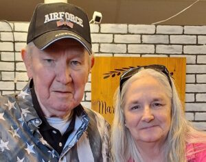 A man wearing a veteran's ballcap with his wife next to him