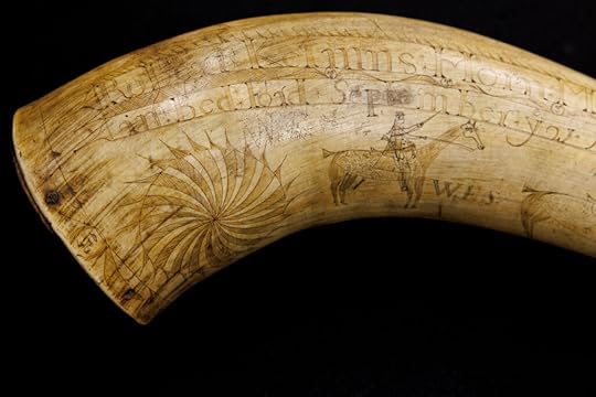 A curved, amber-colored cow horn, beautifully engraved with the name Robert Kelmn and a much less sophisticated etching of a man on a horse below the name.