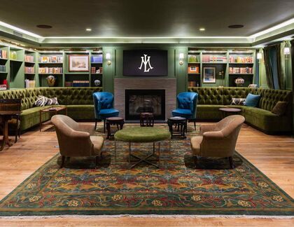 Cozy reading nook with green velvet chairs and a fireplace, surrounded by bookshelves in the Mercantile Library.