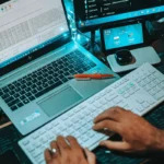 Tech-savvy workspace showing coding activity across a laptop, keyboard, and monitors.