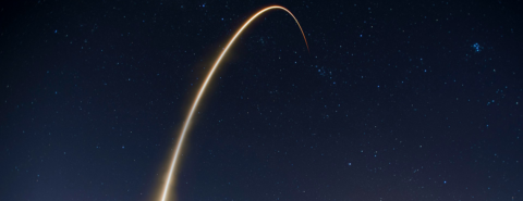 Image depicts the arc of a SpaceX rocket launch set against the night sky