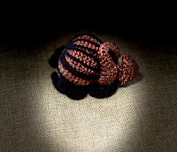 a crocheted beetle, black and rusty/bronze