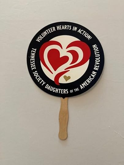 A handheld fan with a wooden handle displays two red hearts and a small gold heart in the center. Surrounding the hearts, white text reads 'Volunteer Hearts in Action! Tennessee Society Daughters of the American Revolution.'.
