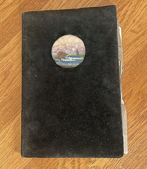 An old photo album with a black velvet cover and a small circle with a watercolor painting of the seaside.