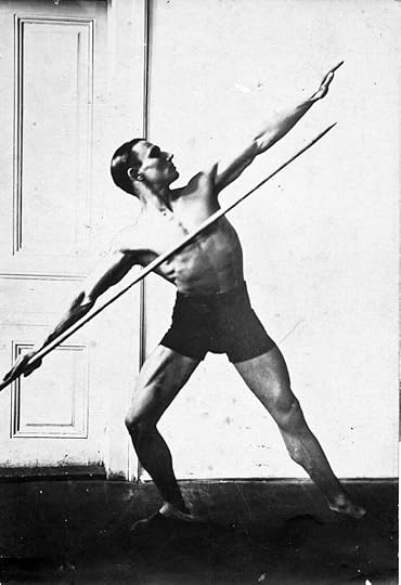 A handsome young man taking a gymnastic pose with a javelin.