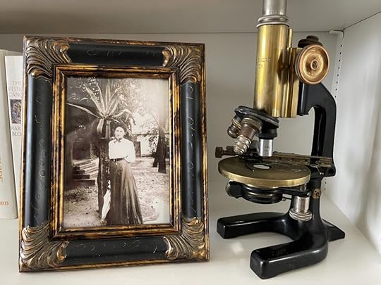 Old photo of a young woman in nineteenth century dress in an ornate frame next to an old microscope of brass and black enamel.