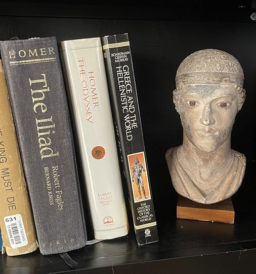 Books about ancient Greece on a bookshelf with a small bust of the Charioteer.