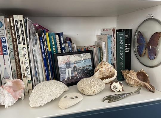 Book shelf with science books, a photo of a man and his son at the beach and various shells and coral.