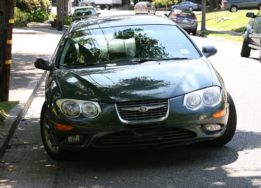 A green car parked in the shade on a rural street.