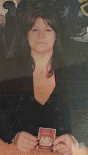 I'm a white woman with long brown hair, sitting at a desk. I've got a stern expression on my face, and am holding a photocopied cover of a passport,.