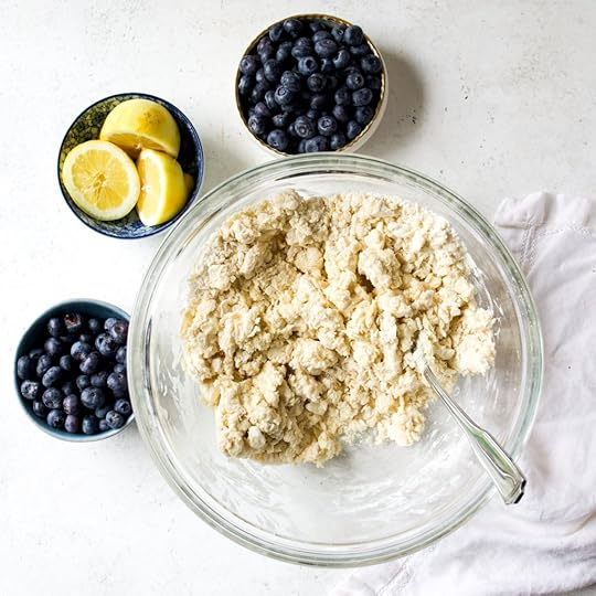 A bowl with just mixed scone dough with smaller bowls of blueberries and lemon halves. 