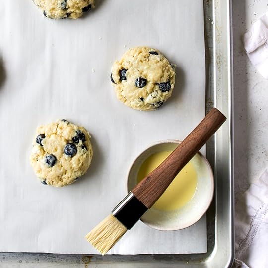 Little blueberry scones on top of a baking sheet with egg wash over the tops.