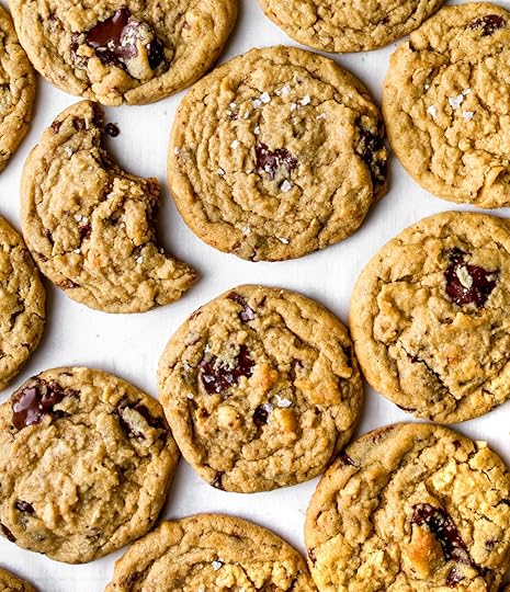 A bunch of cookies on a white surface; one with a bite out of it.