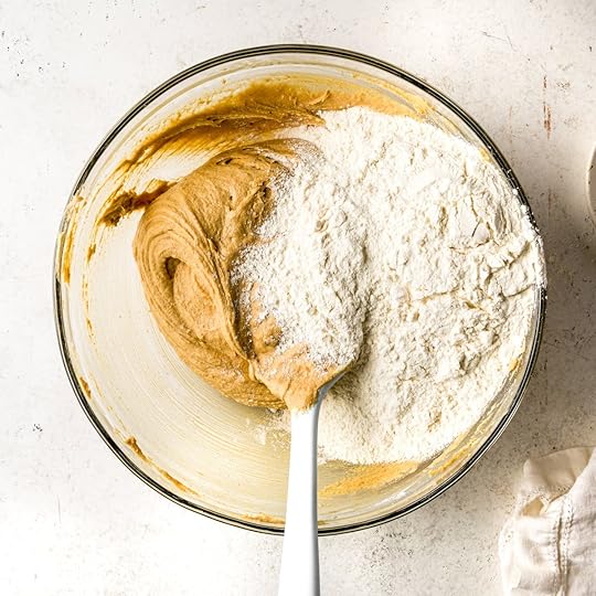 A bowl on a white surface with flour on top of cookie dough.