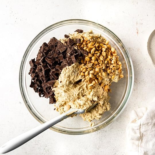 Peanut butter cookie dough with chocolate chunks and roasted, salted peanuts in a glass bowl.