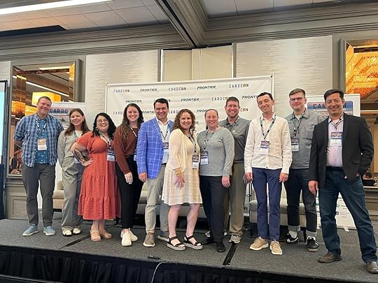 A group of eleven people is standing on a stage in front of a backdrop with logos that read