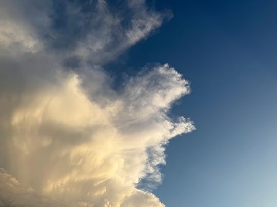 The image shows a sky with large, fluffy clouds on the left side, illuminated by sunlight, creating a bright, golden appearance. The sky transitions to a clear blue on the right side, with the clouds appearing to dissipate as they move across the image.